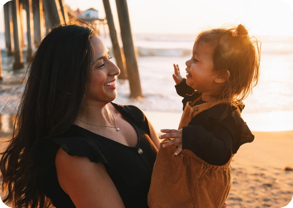 Dr. Aimee VanDerschelden, DC holding a small child on the beach beneath Huntington Beach Pier