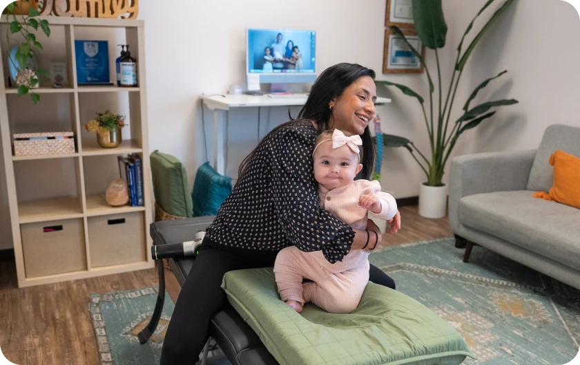 A mother holding her baby in a Momma's Chiro treatment room, with toys and a play mat on the floor